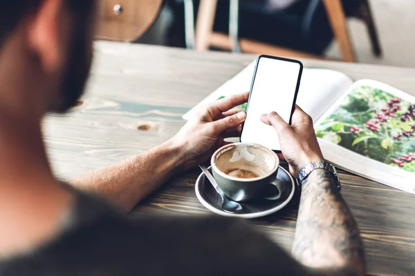 Homem usa smartphone e livro de leitura com café à mesa no café — Fotografia de Stock