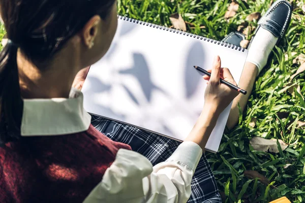 Frau mit Bleistift auf Notizbuch im Park auf Gras sitzend — Stockfoto