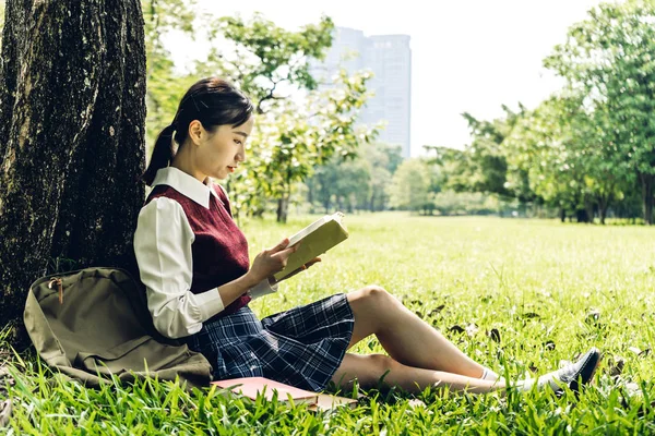 アジアの女子学生は、木の下に座ってノートブックを読んでリラックス — ストック写真