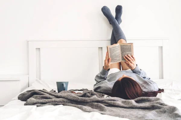 Young woman relaxing and reading book on bed at home — Stock Photo, Image