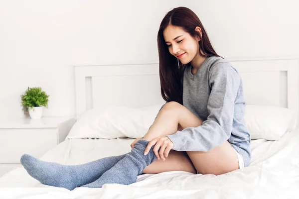 Woman sit on the bed wearing and putting on long warm socks in c — Stock Photo, Image