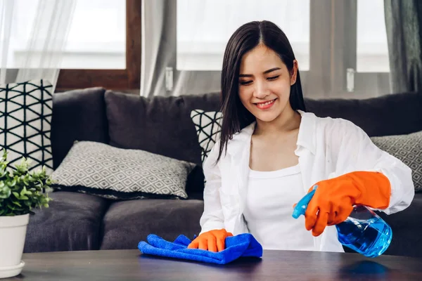 Giovane donna con guanti protettivi usando uno spray e uno straccio mentre cerchio — Foto Stock