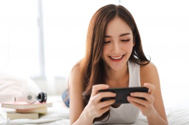 Mutlu kadın kullanarak ve smartphone tarafından yatağa konuşmak rahatlatıcı 