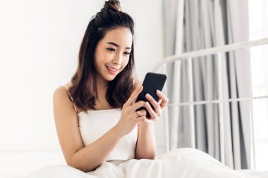 Mutlu kadın kullanarak ve smartphone tarafından yatağa konuşmak rahatlatıcı 