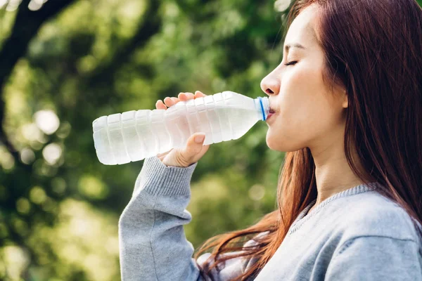 Linda mulher asiática bebendo água de uma garrafa enquanto relaxa — Fotografia de Stock