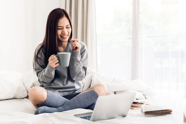 Νεαρή γυναίκα που χαλαρώνει και πίνει φλιτζάνι ζεστό καφέ ή τσάι χρησιμοποιώντας — Φωτογραφία Αρχείου