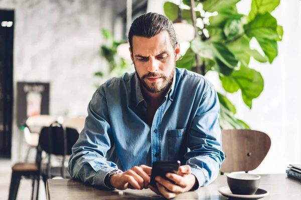 Bonito homem hipster barbudo usar smartphone com café na mesa — Fotografia de Stock