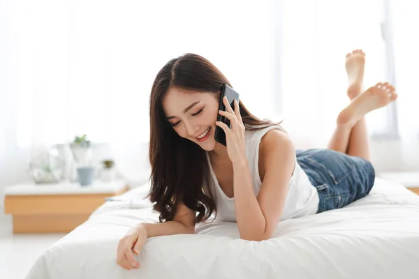 Gelukkige vrouw ontspannende gebruiken en praten door de smartphone op het bed — Stockfoto