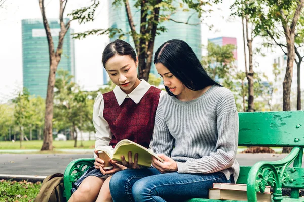 Two smiling international students or teenagers sitting and read