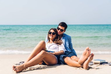 Hindistan cevizi suyu içen ve tropik plajda kitap yazan genç bir çift.