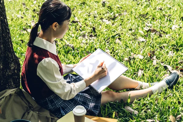 Trの下に座っているノートにペンを書いてリラックスする女性 — ストック写真