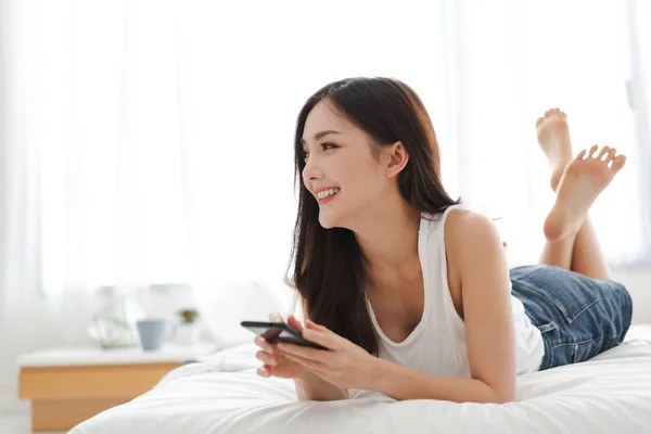 Mujer feliz relajante usando y hablando por teléfono inteligente en la cama —  Fotos de Stock