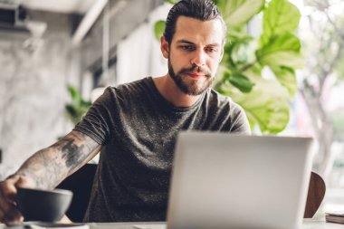 Yakışıklı sakallı hipster adam kullanımı ve dizüstü bilgisayar bakıyor 