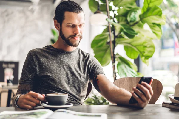 Bonito homem hipster barbudo usar smartphone com café na mesa — Fotografia de Stock