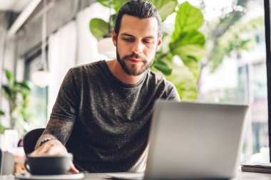 Yakışıklı sakallı hipster adam kullanımı ve dizüstü bilgisayar bakıyor 
