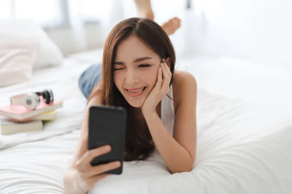 Mulher feliz relaxante usando e falando por smartphone na cama — Fotografia de Stock