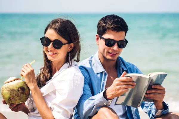 Jovem casal com suco de coco e livro na praia tropical. — Fotografia de Stock