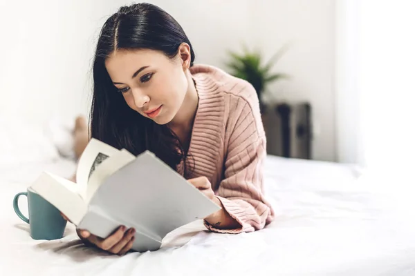 Giovane donna rilassante e lettura libro sul letto a casa — Foto Stock