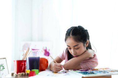 Okulda okuyan küçük bir kız, evde kalem yapıp not defterine yazıyor. Eğitim konsepti.