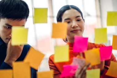Gündelik yaratıcı mutlu iki gülümseme Asyalı iş adamları strateji analizi ve beyin fırtınası planlıyorlar. Çıkartma yapıştırmaları yapıştırıyorlar ve modern ofisin cam tahtasında başlangıç projesi için fikir paylaşıyorlar.