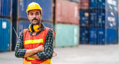 Kasklı profesyonel mühendis konteynır ustabaşı ayakta çalışıyor ve elinde telsiz ile Camara 'ya bakıyor. Lojistik ve iş ihracatı.