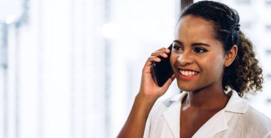 Gülümseyen profesyonel iş kadını Afro-Amerikan siyahi kadın ofiste çalışıyor ve akıllı telefon kullanıyor.