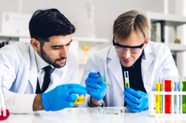 Profesyonel iki bilim adamı test tüpünde sıvı analiz ederken ve karıştırırken kimyasal bir deney yapıyor. Genç bilim adamı laboratuvarda cam üzerine kimyasal örnekler bırakıyor.