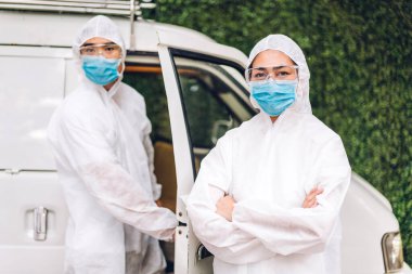 Koruyucu maske takan dezenfekte işçileri ve müşteri evindeki Coronavirüs 'ü öldürmek için beyaz takım elbise dezenfektan sprey temizlik virüsü kullanan profesyonel ekipler.