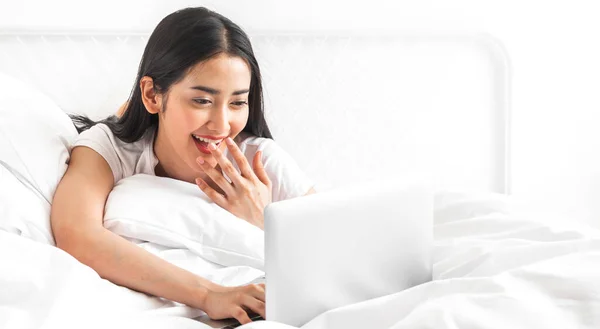 Young asian woman relaxing using laptop computer on bed in the bedroom at home.Young beauty girl working and typing on keyboard at home.work from home concept