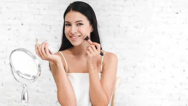 Smiling of young beautiful pretty woman clean fresh healthy white skin looking at camara.girl holding make-up brushes and make up on face with cosmetics set at home.facial beauty and cosmetic concept