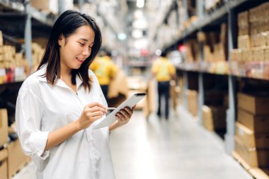 Gülümseyen Asyalı yönetici kadın portresi ayakta duruyor ve malzeme ve gereçleri depoda kontrol etmek için tablet bilgisayardan ayrıntılı talimat veriyor. Lojistik ve iş ihracatı