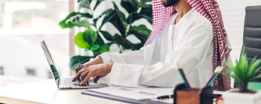 Laptop bilgisayar izleme teknolojisine bakan yakışıklı, kendine güvenen Arap işadamı. Modern iş yerinde düşünen ve planlayan Arap iş arkadaşları.