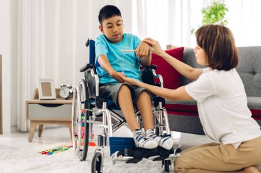 Asyalı fizyoterapistin portresi engelli çocuk sağlığı sorununa rehabilitasyon kliniğinde tekerlekli sandalyede oturarak yardım ve oyun oynayarak yardımcı oluyor.