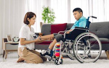Asyalı fizyoterapistin portresi engelli çocuk sağlığı sorununa rehabilitasyon kliniğinde tekerlekli sandalyede oturarak yardım ve oyun oynayarak yardımcı oluyor.
