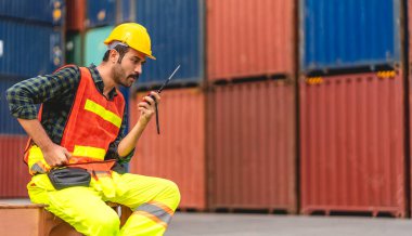 Miğferli profesyonel mühendis konteynır ustabaşı ayakta çalışıyor ve telsiz kullanıyor stokları yükleme için konteynıra koyuyor. Lojistik ve iş ihracatı