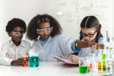 Okuldaki deney laboratuarında test tüpünde sıvı karıştırırken ve analiz ederken araştırma yapmayı öğrenen ve kimyasal deney yapan bir grup küçük sevimli öğrenci. Eğitim.