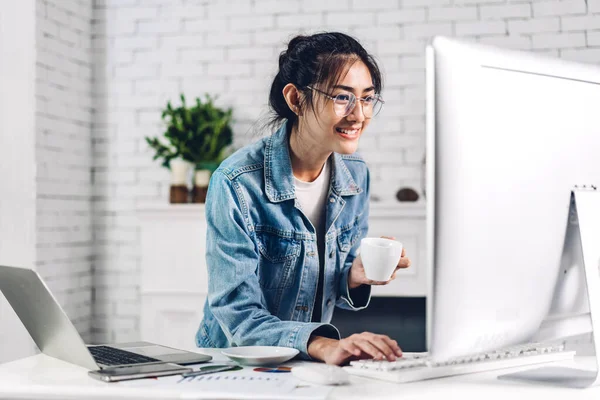 Young smiling happy asian woman relaxing using desktop computer working and video conference meeting online chat.Young creative girl drink coffee at home.work from home concept
