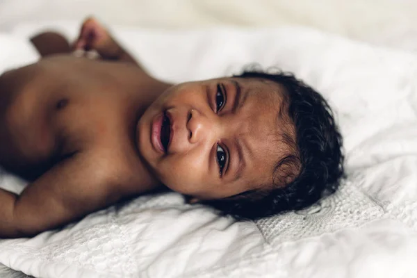 ポートレートのかわいいですかわいいですアフリカ系アメリカ人の赤ん坊見ますカメラでAホワイトベッドルーム — ストック写真