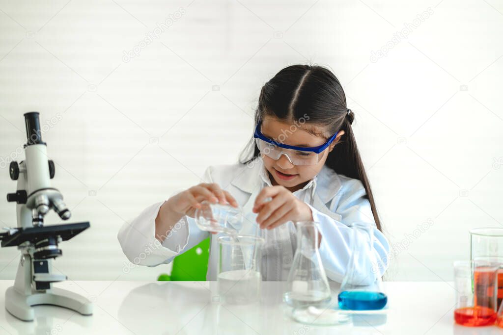 Cute little girl student child learning research and doing a chemical experiment while making analyzing and mixing liquid in glass at science class on the table.Education and science concept