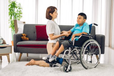 Asyalı fizyoterapistin portresi engelli çocuk sağlığı sorununa rehabilitasyon kliniğinde tekerlekli sandalyede oturarak yardım ve oyun oynayarak yardımcı oluyor.