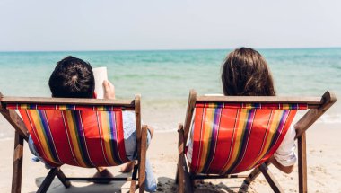 Romantik aşıklar. Genç mutlu çift kumsalda sarılıp oturur ve denize bakar. Birlikte tropik sahillerde eğlenir ve dinlenir.