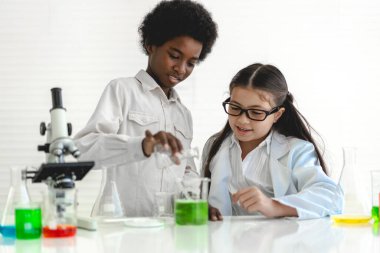 Okuldaki deney laboratuarında test tüpünde sıvı karıştırırken ve analiz ederken araştırma yapmayı öğrenen ve kimyasal deney yapan bir grup küçük sevimli öğrenci. Eğitim.