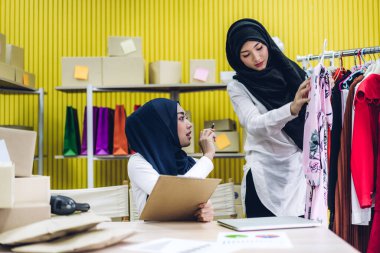 Gülümseyen iki güzel Müslüman kadının portresi Asyalı serbest çalışan bir kadın dizüstü bilgisayarla online alışveriş yapıyor evdeki paket kutusuyla iş yeri çevrimiçi nakliyat ve teslimat.