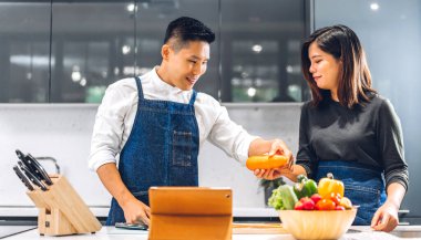 Genç Asyalı çift masada taze sebze salatasıyla yemek yaparken eğleniyor. Mutfakta lezzetli bir yemek hazırlamak için tablet bilgisayarlı ve internette yemek tarifi arayan mutlu çift.