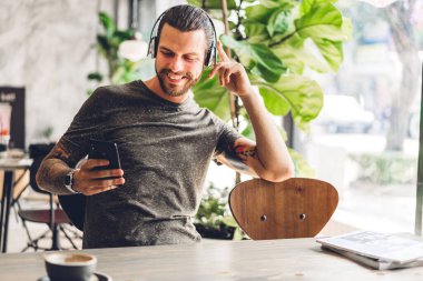 Yakışıklı hippi kahve ile dijital akıllı telefon kullanarak rahatlıyor ve kafeteryada ve restoranda ekran daktilo mesajlarına bakıyor, online ve sosyal medyada oyun oynuyor.