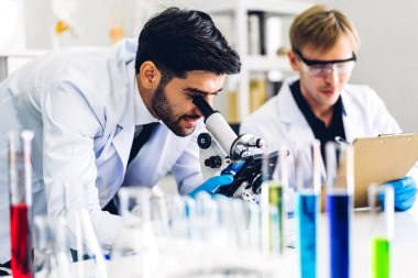 Profesyonel iki bilim adamı test tüpünde sıvı analiz ederken ve karıştırırken kimyasal bir deney yapıyor. Genç bilim adamı laboratuvarda cam üzerine kimyasal örnekler bırakıyor.