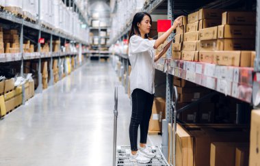 Gülümseyen Asyalı yönetici kadın portresi ayakta duruyor ve malzeme ve gereçleri depoda kontrol etmek için tablet bilgisayardan ayrıntılı talimat veriyor. Lojistik ve iş ihracatı