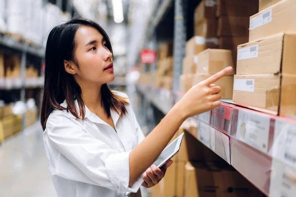 Portrait of smiling asian manager worker woman standing and order details on tablet computer for checking goods and supplies on shelves with goods background in warehouse.logistic and business export