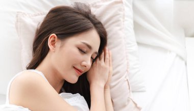 Neşeli, güzel, Asyalı güzel bir kadının gülümsemesi taze, sağlıklı, beyaz bir tenin uykusunu ve gözlerini kapatması. Kız evde dinleniyor ve yatakta eğleniyor.