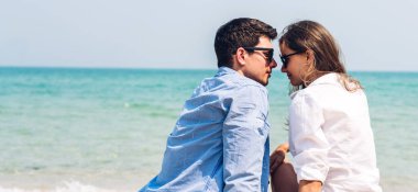 Romantik aşıklar. Genç mutlu çift, tropik plajlara yazı yazdıkları için kumun üzerinde sarılıp denize bakıyor, eğleniyor ve birlikte rahatlıyor.